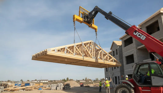 Heavy-duty telehandler truss jib attachment lifting roof trusses at a construction site